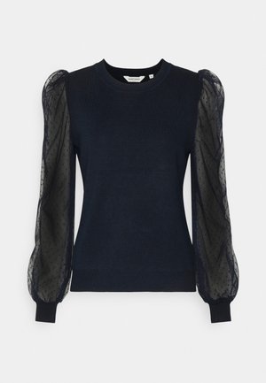 Granatowy sweter z przezroczystymi czarnymi bufiastymi rękawami z subtelnym wzorem w kropki, pokazany na jednolitym białym tle.