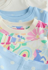 Chemises pour enfants colorées empilées, avec des cols ronds, présentant des motifs de pois, de fleurs, d'arcs-en-ciel et de licornes.