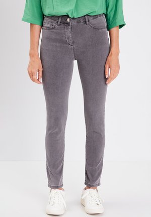 Jean skinny gris avec une texture lisse, design à cinq poches et fermeture à bouton, associés à des baskets blanches et un haut vert.