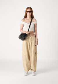 Off-the-shoulder white crop top, beige cargo pants with pocket details, black handbag, and white sneakers. Smooth textures, casual fit.