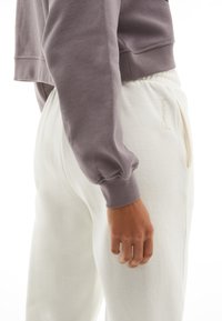 Sweat-shirt court violet clair avec des manches bouffantes, associé à un jogging crème avec poches latérales et une broderie discrète.