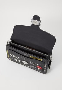 Sac à main en cuir noir avec quincaillerie métallique, présentant des motifs graphiques incluant du texte et des images. L'intérieur comprend une poche zippée.