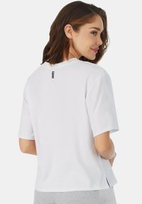 Witte T-shirt met korte mouwen en een ronde halslijn, met een zwart "DKNY" logo nabij de achterkant van de hals en zijsplitten in de zoom.