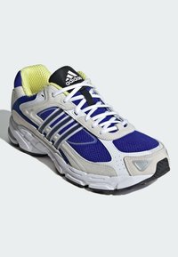 Lila és szürke sportcipő hálós felsőrésszel, fehér fűzőkkel és texturált talppal. Az adidas logó a nyelvén és ezüst csíkok az oldalán találhatók.