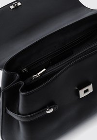 Borsa a tracolla in pelle nera con una texture liscia, con un accento in metallo quadrato argentato, tasca con zip superiore e un design leggermente curvo.