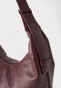 Tumepruun nahast käekott, mille lähedalt vaadates on näha sile tekstuur, lai reguleeritav rihm metallsõrestikega ja ülemine tõmblukk.