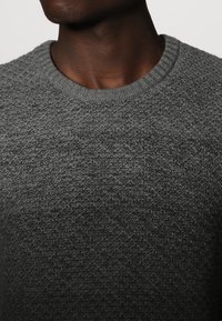 Maglione grigio a maglia con texture, dotato di scollatura rotonda, caratterizzato da un leggero motivo in rilievo e polsini a costine.