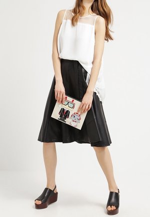 Biały top bez rękawów z przezroczystym panelem; czarna plisowana spódnica z ekologicznej skóry; masywne czarne drewniaki na platformie; trzyma wzorzysty kopertówkę.