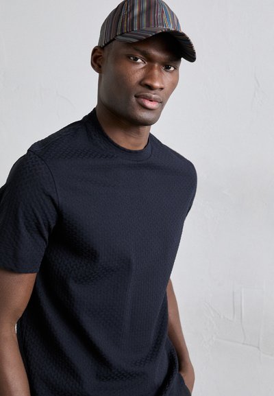 Στρατιωτική μπλούζα κοντομάνικη σε ναυτικό χρώμα με υφασμάτινο σχέδιο και στρογγυλή λαιμόκοψη, συνδυασμένη με ένα καπέλο πολύχρωμο ριγωτό με καμπυλωτή γείσο.