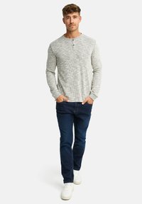 Grå langærmet henley-skjorte med tekstureret mønster, to-knapslukning, kombineret med mørkeblå jeans og hvide sneakers.