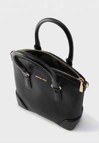 Czarna torba z ziarnistej skóry z dwoma górnymi uchwytami, zamkiem błyskawicznym, złotymi okuciami oraz wytłoczonym logo z przodu. Szeroka podstawa z zaokrąglonymi rogami.