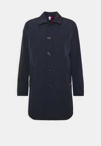 Marineblauer, leichter Mantel mit Stehkragen, Knopfleiste vorne und zwei Seitentaschen. Glatter Stoff mit subtiler Textur und ohne sichtbare Muster.