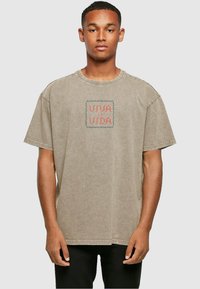 Overdimensjonert beige T-skjorte laget av bomull med rund hals og korte ermer. Har brodert "VIVA LA VIDA" i rødt og blått.