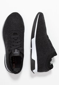 Schwarze Sportsneaker mit einem strukturierten Mesh-Obermaterial, flachen Schnürsenkeln und einer gepolsterten Sohle, die weiße Akzente und ein elegantes Design aufweist.