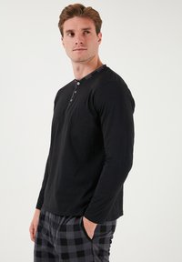 Sort langærmet skjorte med en knaplukning rundt om halsen, parret med grå og sort ternede pyjamasbukser. Stoffet ser blødt ud og har en afslappet pasform.