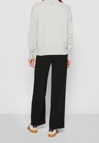 Szary sweter dzianinowy z długimi rękawami i ściągaczem u dołu, w połączeniu z czarnymi szerokimi spodniami i beżowymi sneakersami z czarnymi akcentami.