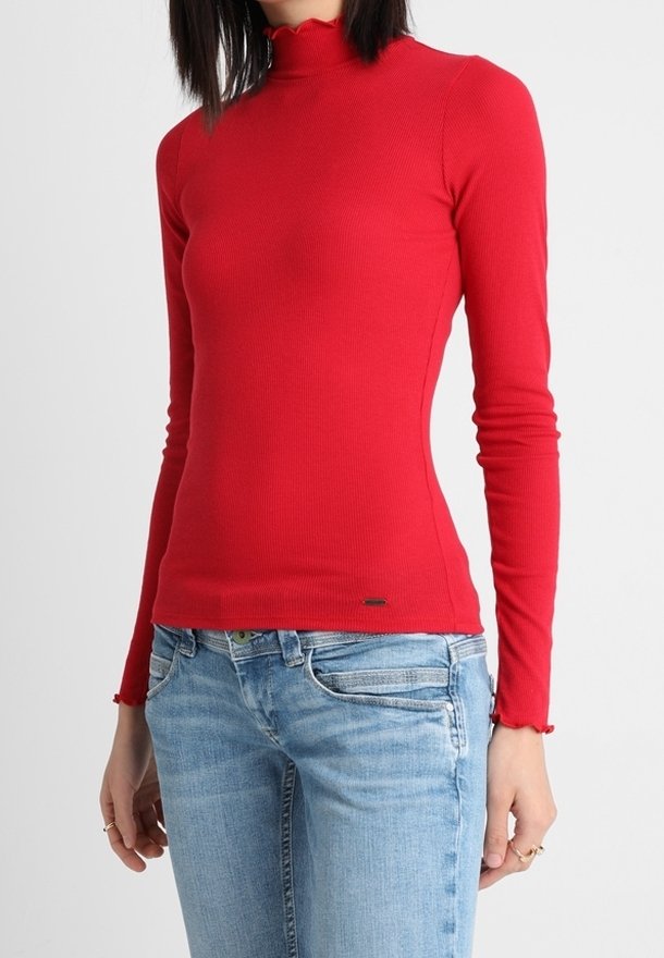 Červený dlouhý rukáv s vroubkovaným rolákem s vyšitým okrajem a slim fit, v kombinaci se světle modrými džíny.