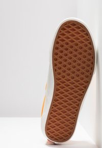 Sneaker mit weißem Canvas-Obermaterial und orangefarbenen Akzenten. Die Gummisohle verfügt über ein strukturiertes Wabenmuster für besseren Grip.