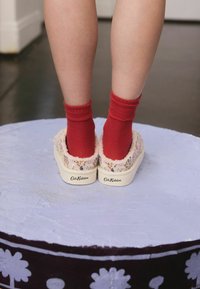 Benen in rode sokken binnen bloemenmotief instap pantoffels staan op een ronde, paarse decoratieve platform.