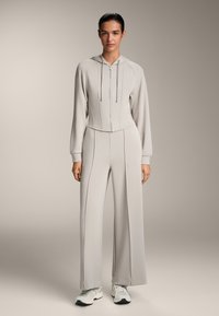 Set athleisure grigio chiaro composto da una felpa corta con zip e pantaloni a gamba larga, con dettagli di cucitura discreti e tessuto leggero.