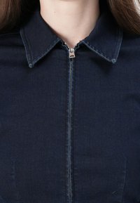 Mørk denimkjole med spiss krage og glidelås foran, med en jevn tekstur og subtile sømdetaljer.