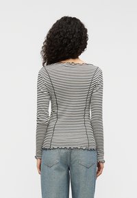 Prúžkované tričko s dlhými rukávmi v čiernej a bielej farbe, s vlnitým výstrihom a lemom, priliehavým strihom a viditeľnými detailmi švov.