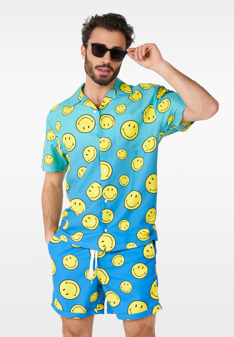 Chemise à manches courtes et shorts assortis en tissu bleu avec imprimé de visages souriants jaunes. Comprend un cordon de serrage blanc sur les shorts.