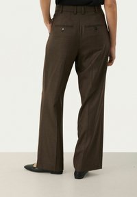 Bordeauxkleurige wijde broek met een gladde textuur, voorzien van knoopzakken aan de achterkant en een getailleerde pasvorm. Gemaakt in combinatie met zwarte ballerina's.