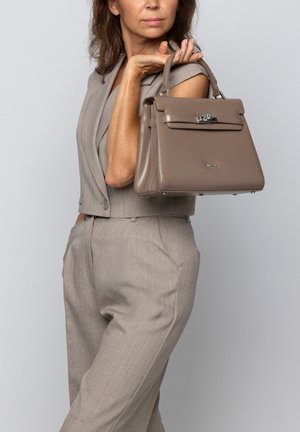 Grijze leren handtas met gestructureerd ontwerp, bovenhandgreep, zilveren hardware accenten en een gladde textuur, vastgehouden door een persoon in een bijpassende outfit.