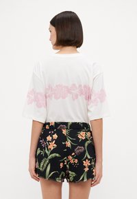 T-shirt en coton blanc avec un imprimé floral rose au dos, associé à un short noir orné de motifs tropicaux vibrants et d'un ourlet effiloché.