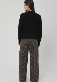Pull en tricot noir à encolure ronde, associé à un pantalon à jambes larges avec un motif animalier marron et noir.