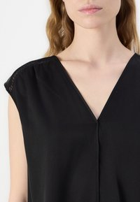 Blusa nera con scollo a V, maniche a farfalla e dettagli in pizzo sulle cuciture delle spalle. Tessuto morbido con una texture liscia e una vestibilità ampia.