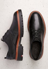 Scarpe in pelle nera con punta arrotondata, sottopiede in legno marrone e suola esterna in gomma nera con grip testurizzato e dettagli in rilievo.