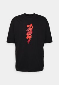 Camiseta negra de gran tamaño con un diseño gráfico vertical rojo con formas angulares en el centro delantero.