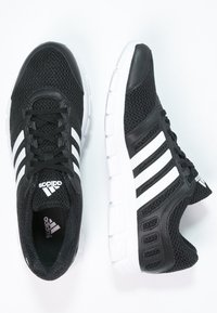 Černé sportovní boty s mřížkovou svrchní částí, třemi bílými pruhy a bílou polstrovanou podrážkou. Mají kulatou špičku a šněrovací design.