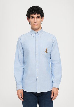 Lichtblauw overhemdd met een zak en een geborduurd hondontwerp, gemaakt van een katoenachtige stof, met lange mouwen en knoopmanchetten.