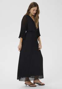 Čierne maxi šaty s plisovaním a priehľadnými rukávmi, dizajn so špicatým výstrihom a gumičkovým pásom. V kombinácii s čiernymi žabkami s priesvitnou textúrou.