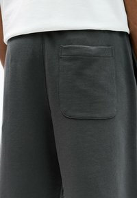 Dark grey cotton sweatpants featuring a back pocket with a rectangular flap. Smooth texture and relaxed fit.