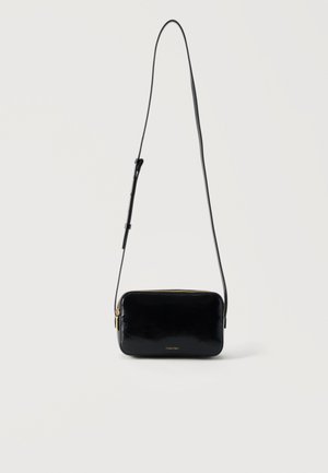 Small black rectangular crossbody bag with a long adjustable strap and gold zipper, Calvin Klein logo on front.