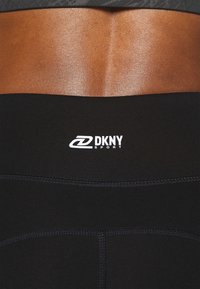 Černé atletické legíny se sportovním logem DKNY v bílé barvě, vyrobené z hladké elastické látky a s viditelnými švy.