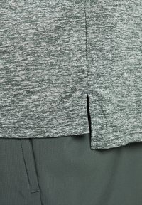 Top de manga corta en gris y verde jaspeado con aberturas laterales, combinado con una parte inferior en verde oscuro sólido. Tejido texturizado con un acabado suave.