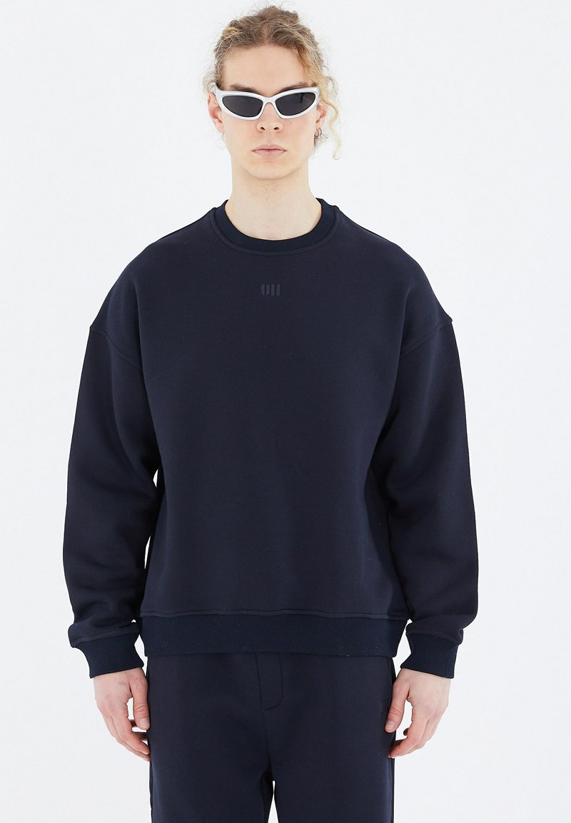 Navy Sweatshirt mit lockerer Passform, gerippten Bündchen und Saum, rundem Ausschnitt und dezentem, tonal gehaltenem Logo auf der Brust. Glatte Textur.