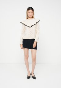 Knit sweater in off-white with a ruffled collar edged in black. Features a cable pattern, paired with a navy pleated skirt and black heels.