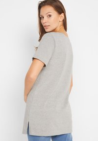 T-shirt in cotone grigio con maniche corte, vestibilità ampia e spacchi laterali sull'orlo, che presenta un design semplice e privo di decorazioni.