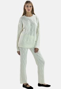 Pull en laine blanc tricoté en câble et pantalon assorti. Texture douce, coupe ample et encolure large. Des ballerines noires complètent la tenue.
