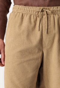 Pantalon en velours côtelé beige avec une taille élastique, doté d'un système de fermeture à cordon et d'une texture à côtes verticales.