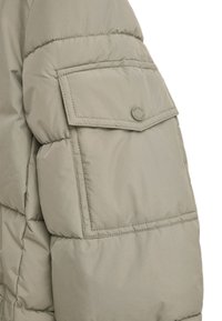 Giacca imbottita a maniche corte in khaki chiaro con una grande tasca a patta e dettaglio del logo rotondo. Materiale sintetico liscio con dettagli cuciti.