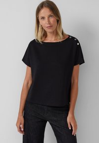 Zwarte T-shirt met korte mouwen, gemaakt van zachte stof, met een ronde halslijn en drie decoratieve zilveren knopen op de linker schouder.