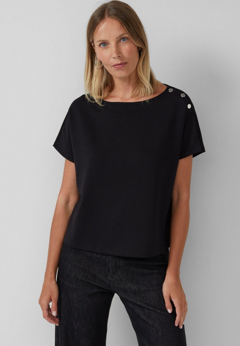 Zwarte T-shirt met korte mouwen, gemaakt van zachte stof, met een ronde halslijn en drie decoratieve zilveren knopen op de linker schouder.