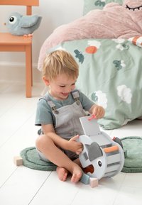 Jong kind zittend op de vloer, spelend met een houten speelgoed in de vorm van een olifant en kleurrijke blokken in een gezellige slaapkameromgeving.